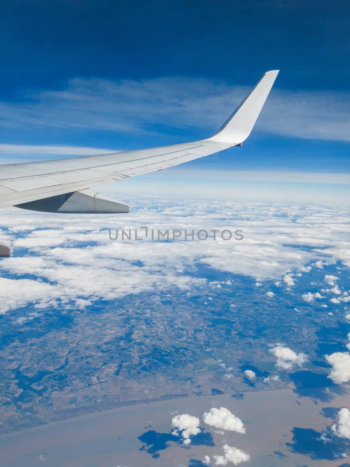 Wing of a commercial airplane flying above a coastal region.