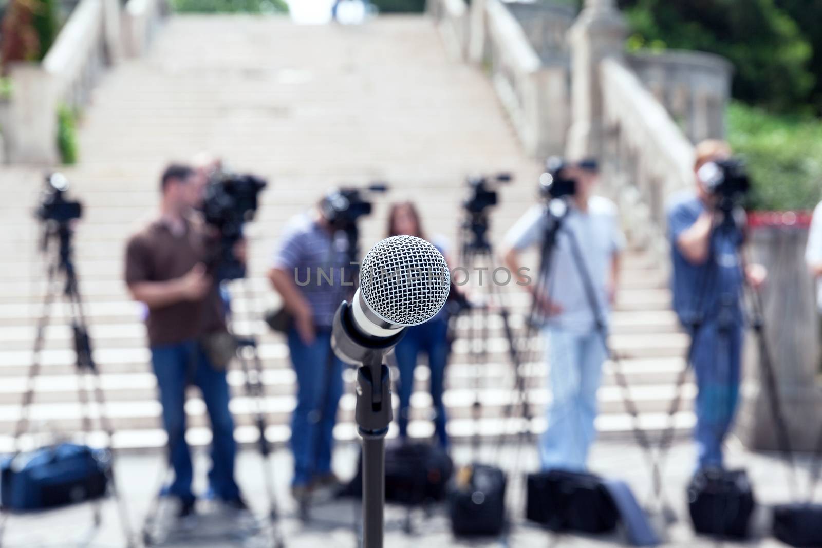 Microphone in focus against blurred camera operators and journalists. News conference.