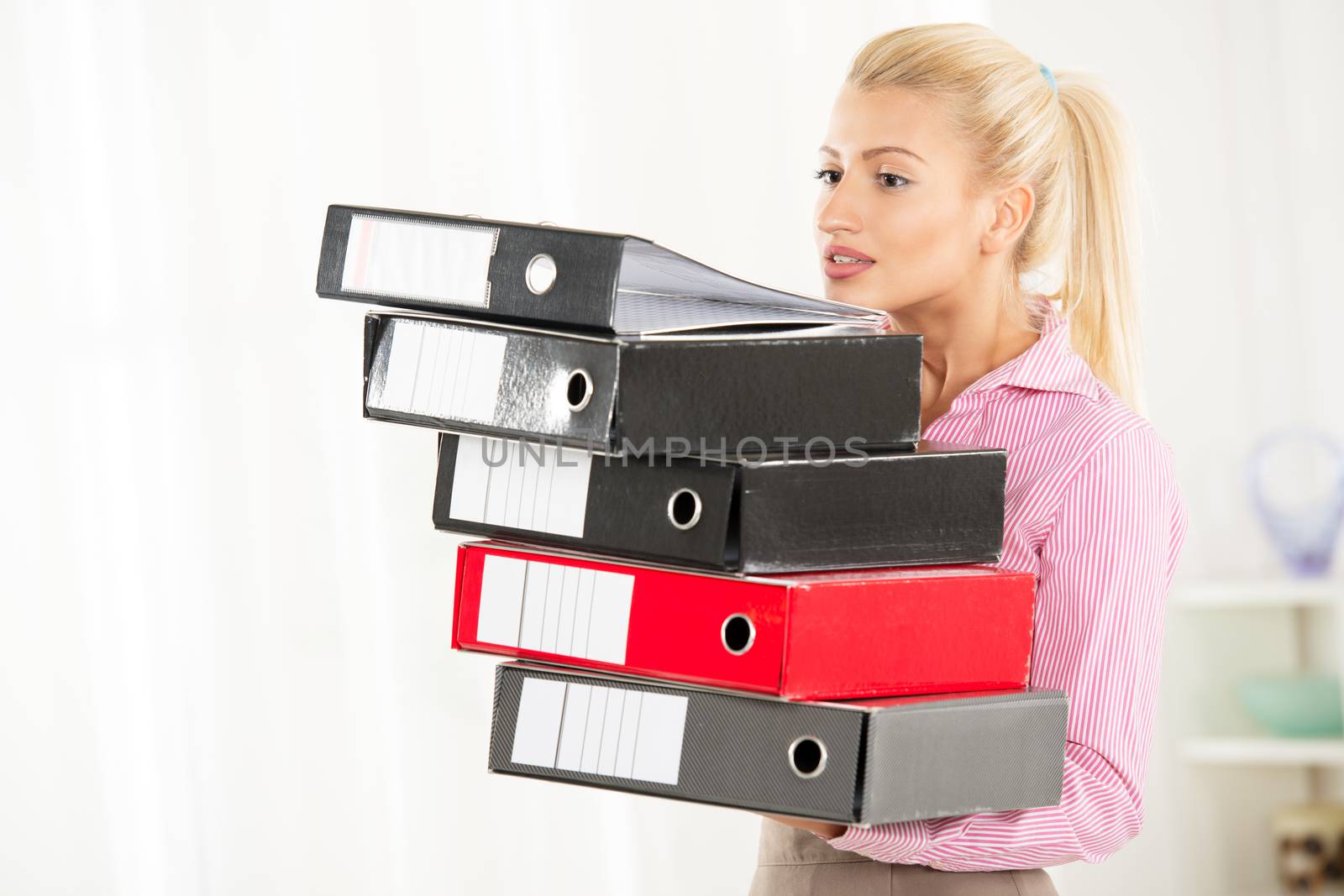 Young blonde woman wearing a stack of binders in the hands, holding them with jaw.