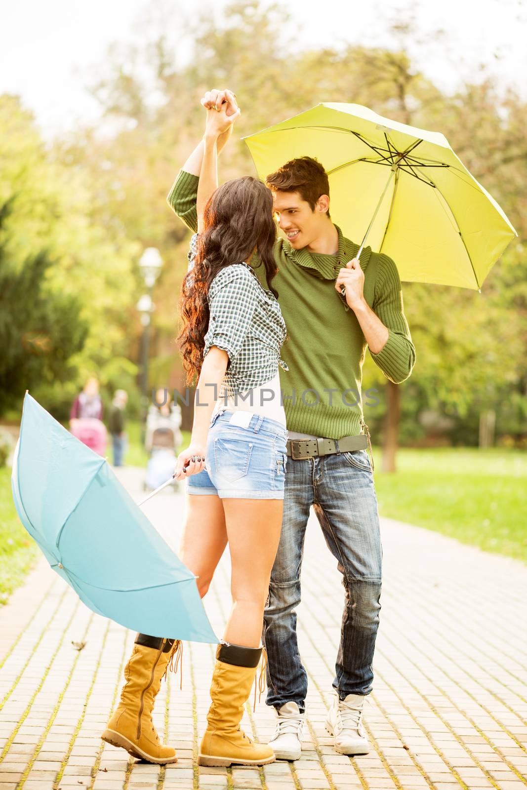 Young couple in love, dancing in the park with umbrellas in hands.