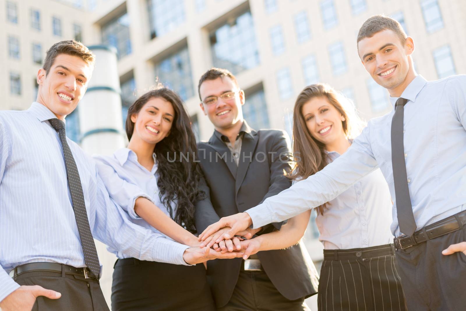 Small group of young business people standing in front of the company with folded hands, motivating for new business wins. With a smile, looking at the camera.