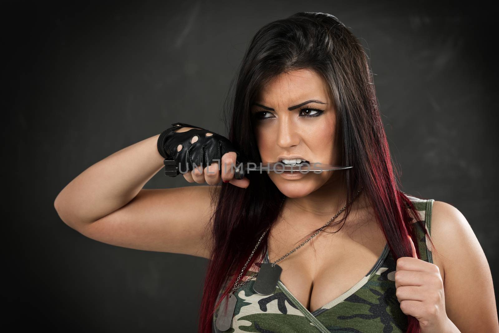 Young beautiful military woman holding bayonet in the teeth