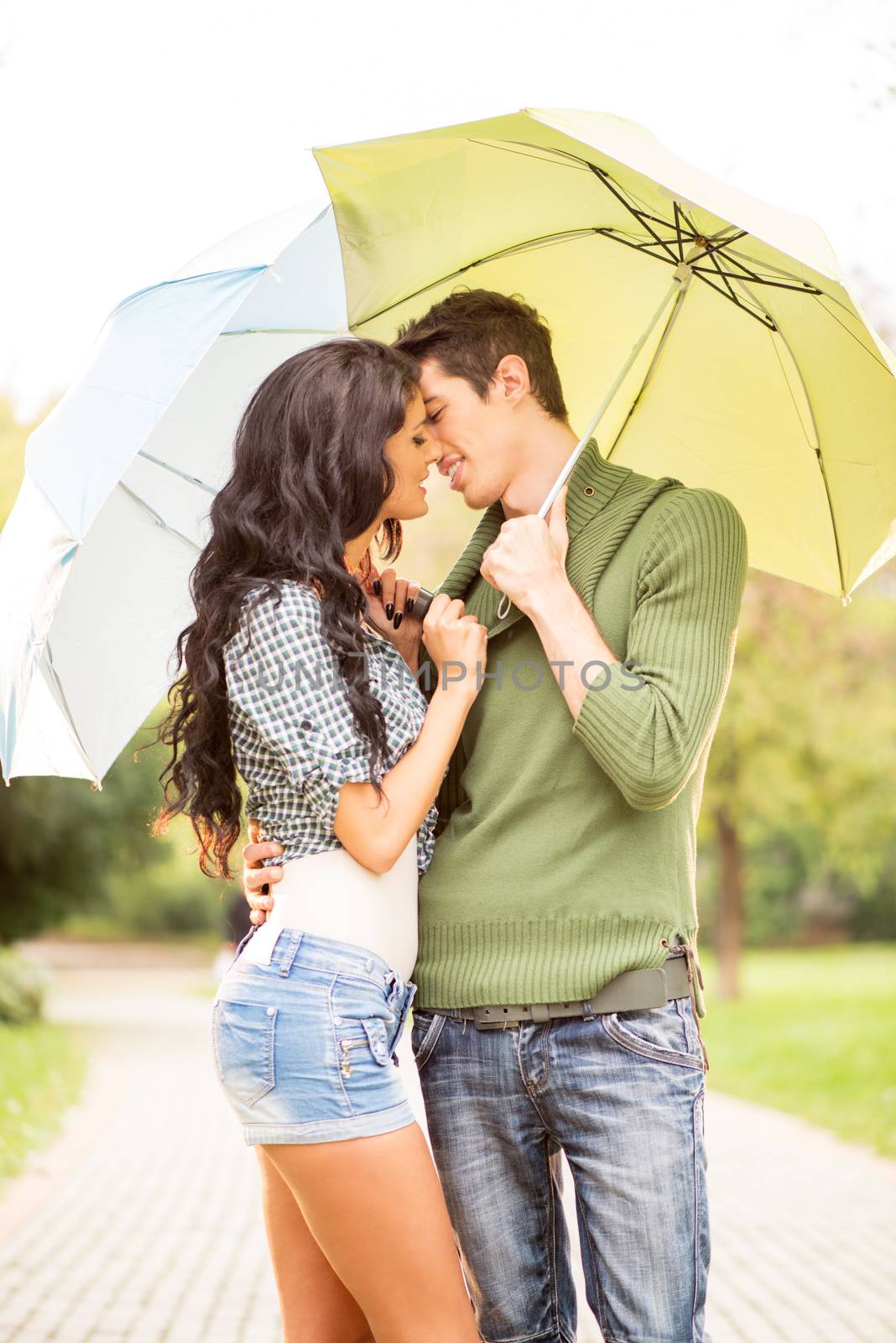 Young boy and girl standing embracing under umbrellas and they kiss.