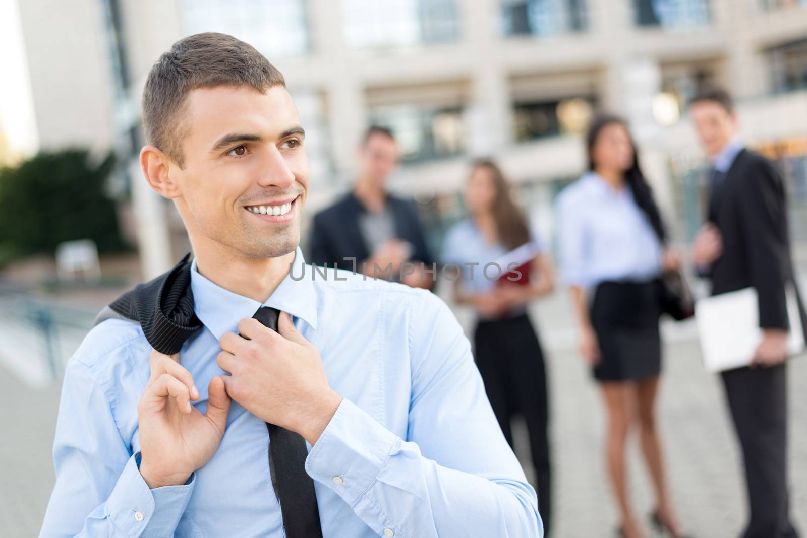 Close- up of a young smiling businessman while standing in front of office building separated from the rest of the business team.