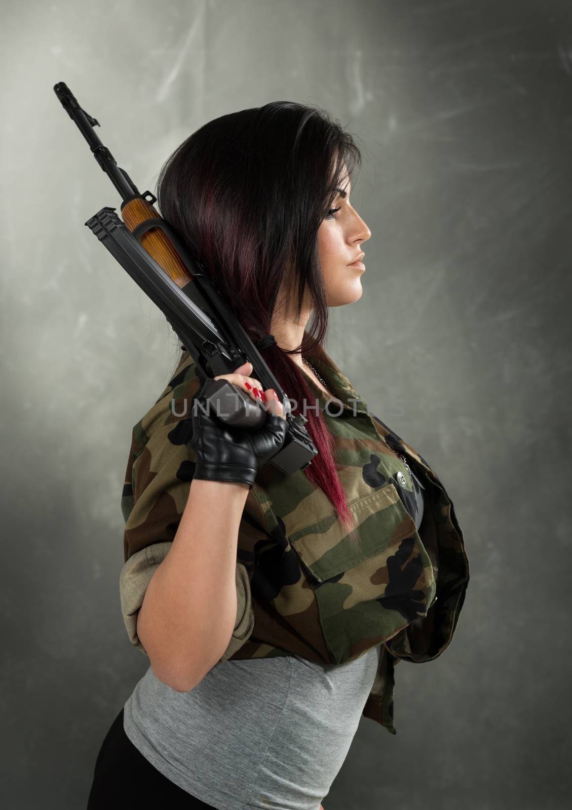 Profile of an attractive young women in military camouflage shirt with a Kalashnikov in her hand.