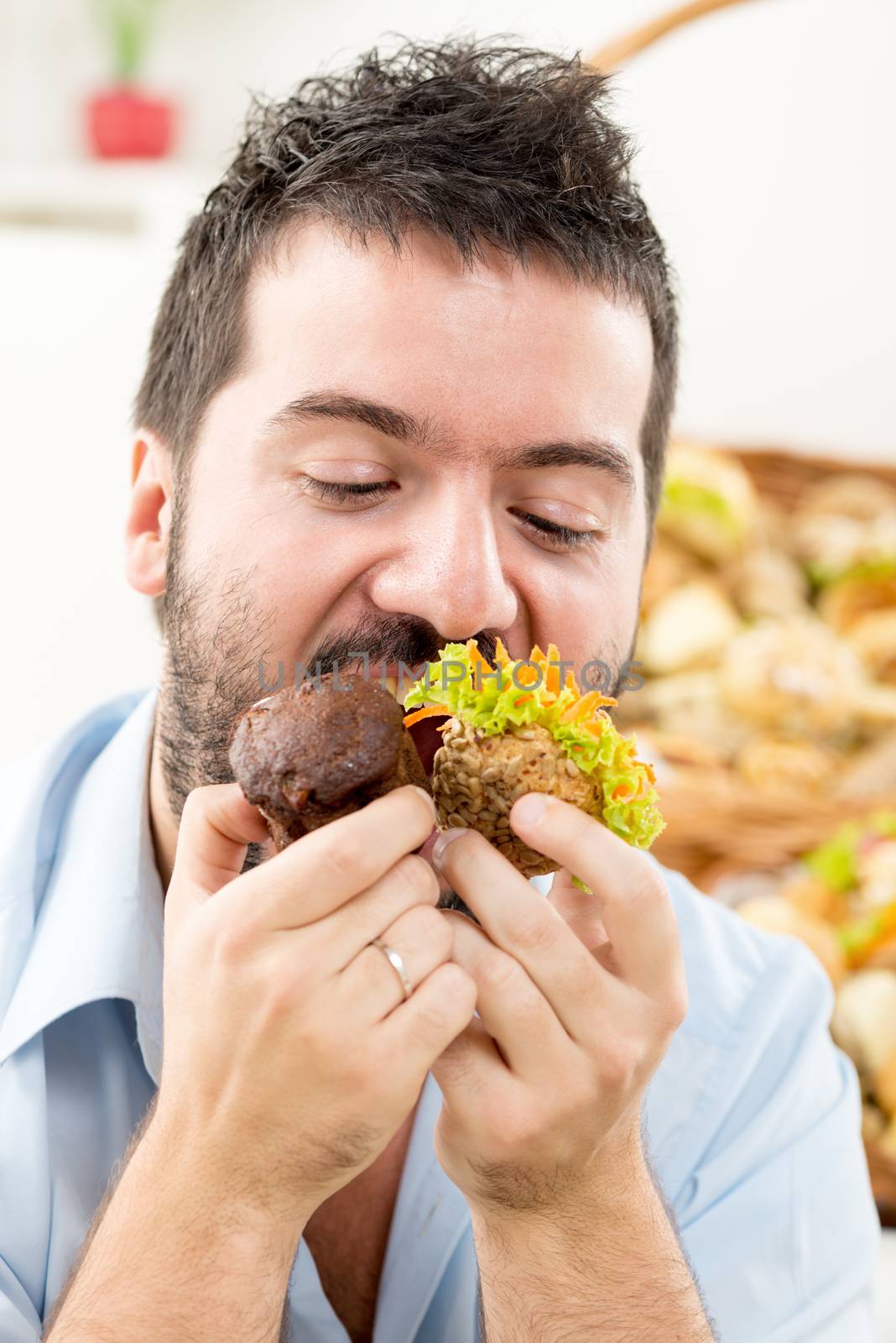 Close-up of a young man with a beard who greedily pushed into the mouth pastries. In the background is woven basket with pastries.