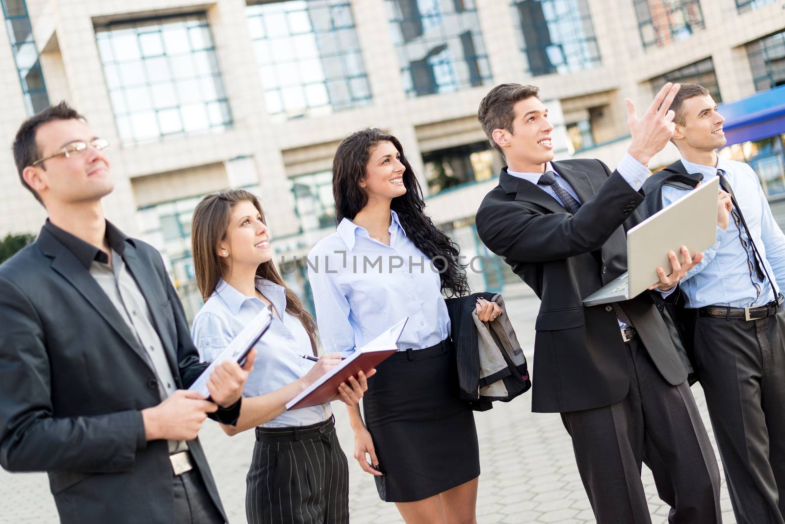 Young businessman with laptop in front of office building outstretched fingers of the hand, aimed at heights, explaining his colleagues business plan.