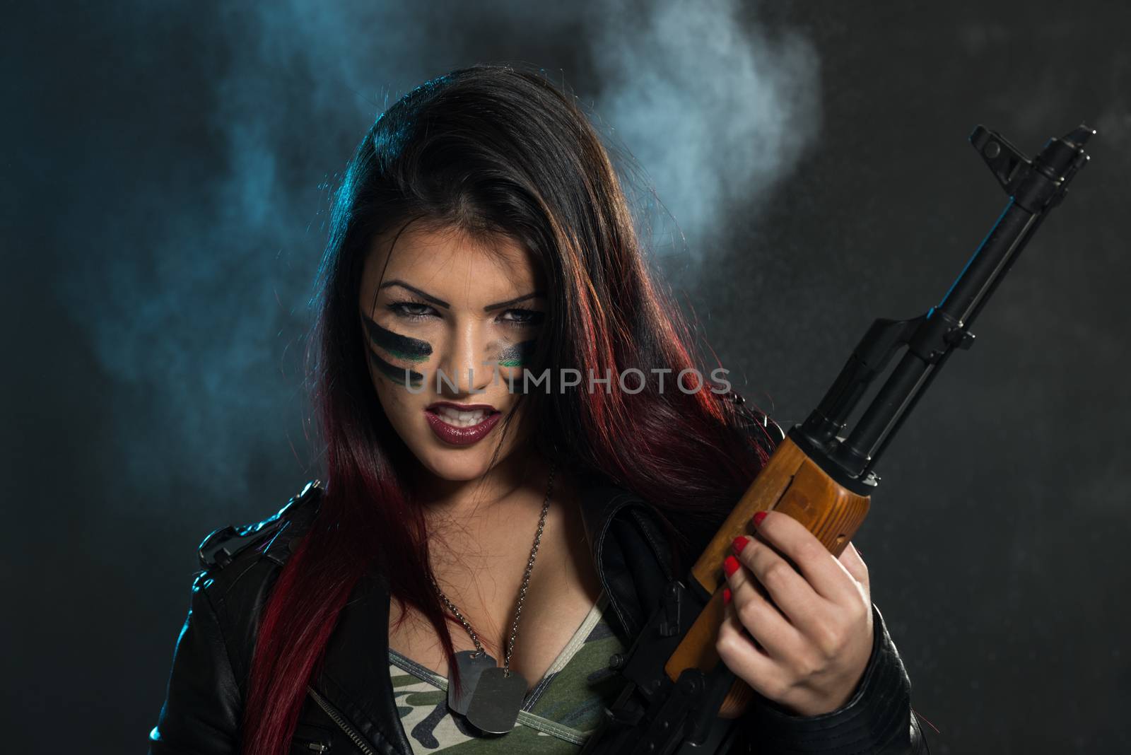 Attractive brunette with an automatic rifle, with war paint on her face and a dangerous expression with clenched teeth, looking at the camera.