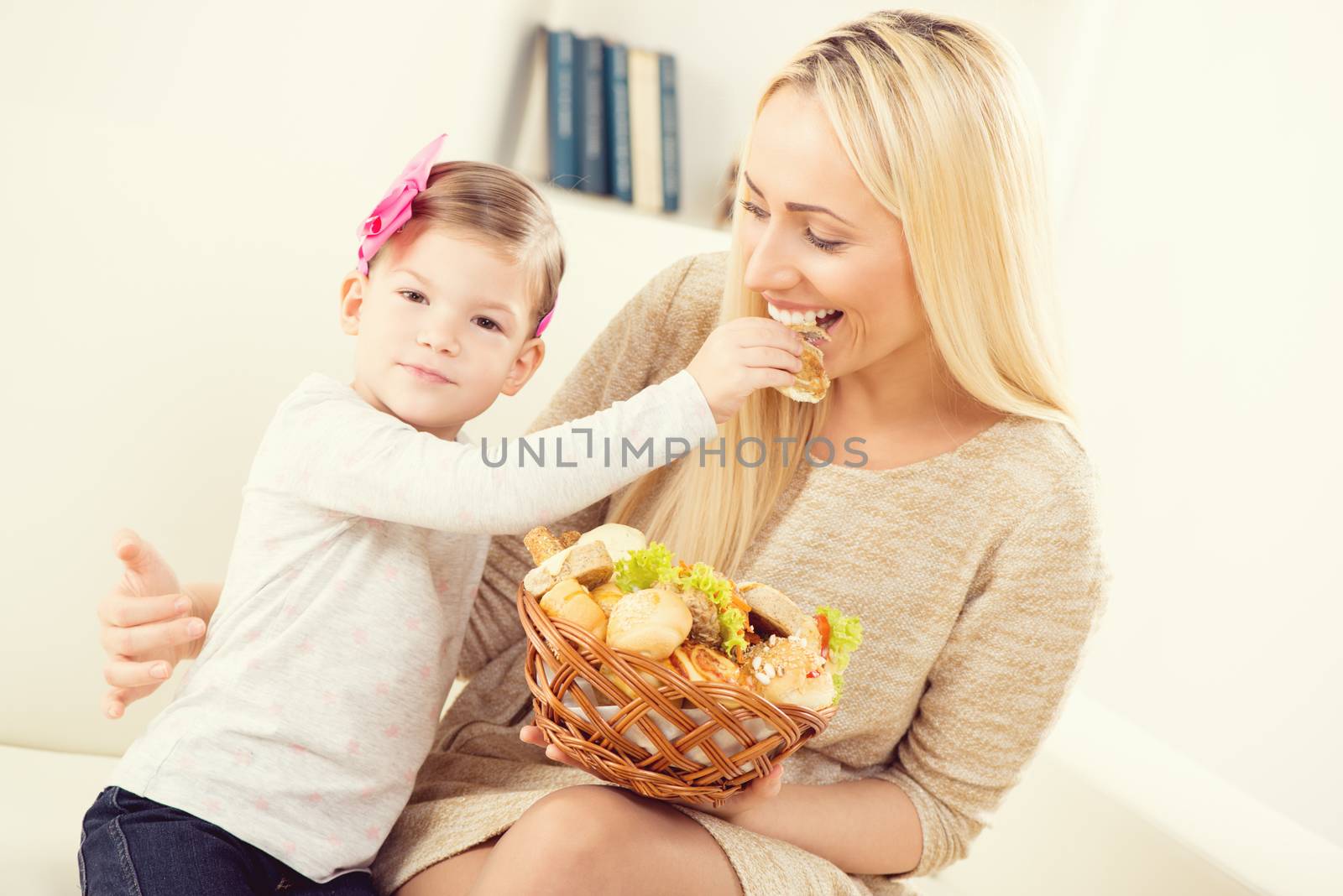 Cute little girl feeding pretty mom with pastries from woven baskets.