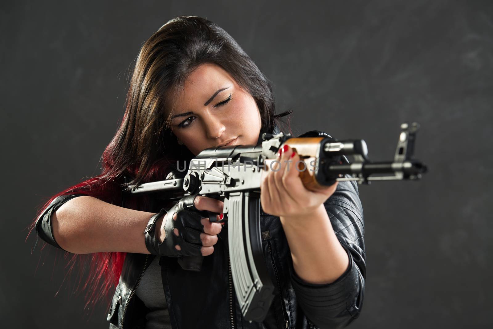 Attractive girl standing in the attitude of aiming and looking through the sight automatic rifle.
