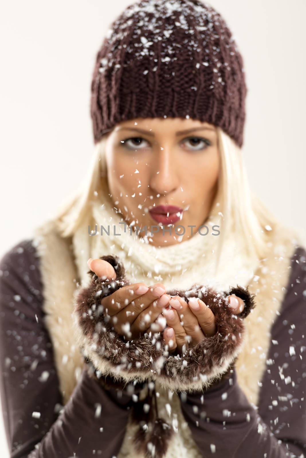 Beautiful young blonde girl In winter clothes, blowing snowflakes In the viewer. The focus is on the hands with snow.