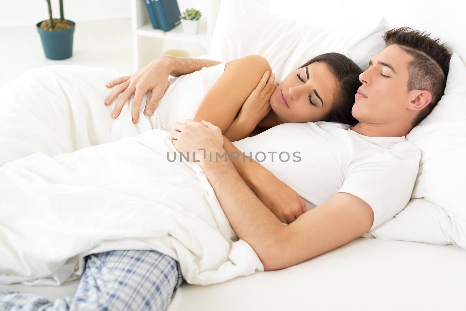 Young heterosexual couple, sleep embracing in bed.