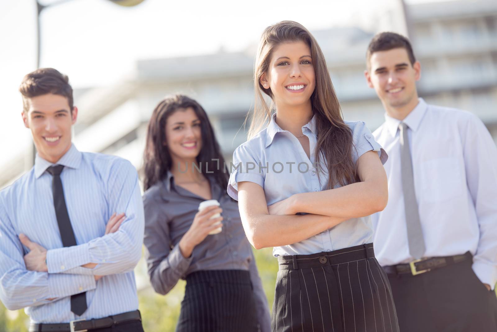 Group of young business people elegantly dressed standing outside enjoying the beautiful day, with a smile looking at the camera.