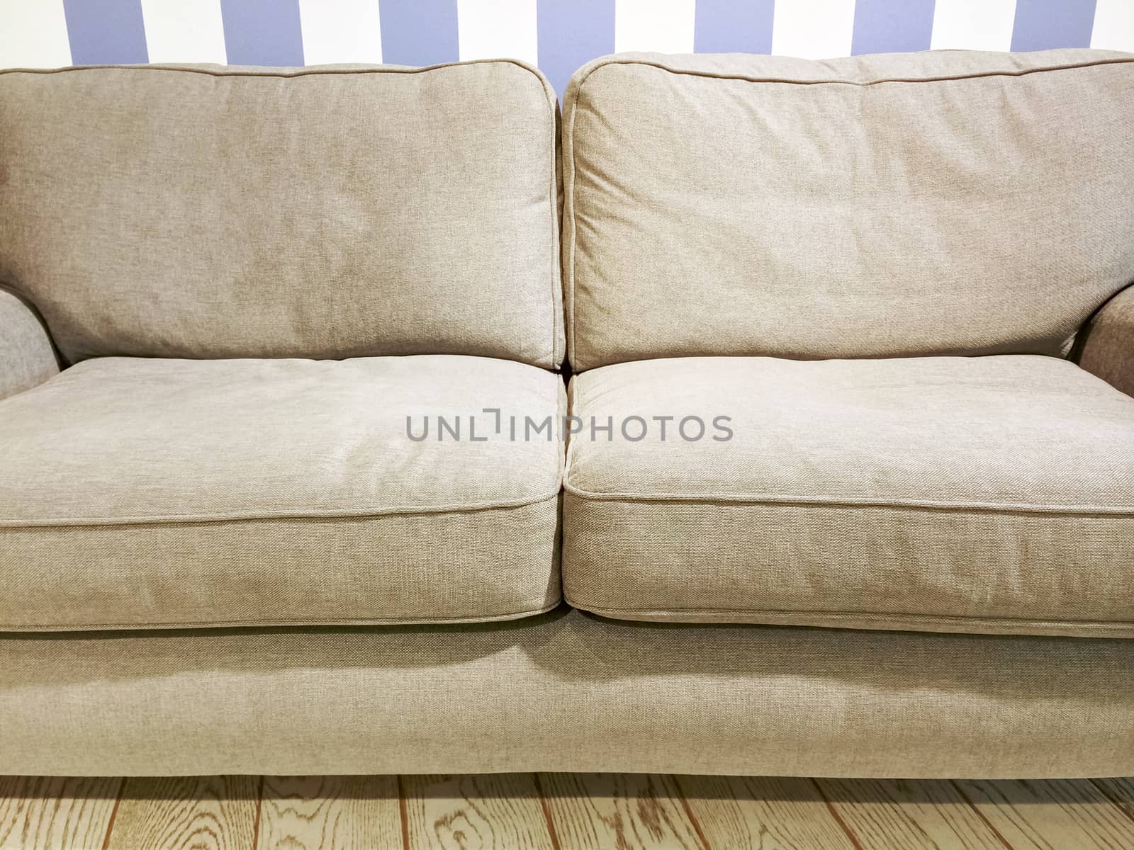 Soft beige sofa near the wall with striped wallpaper. Comfortable furniture.