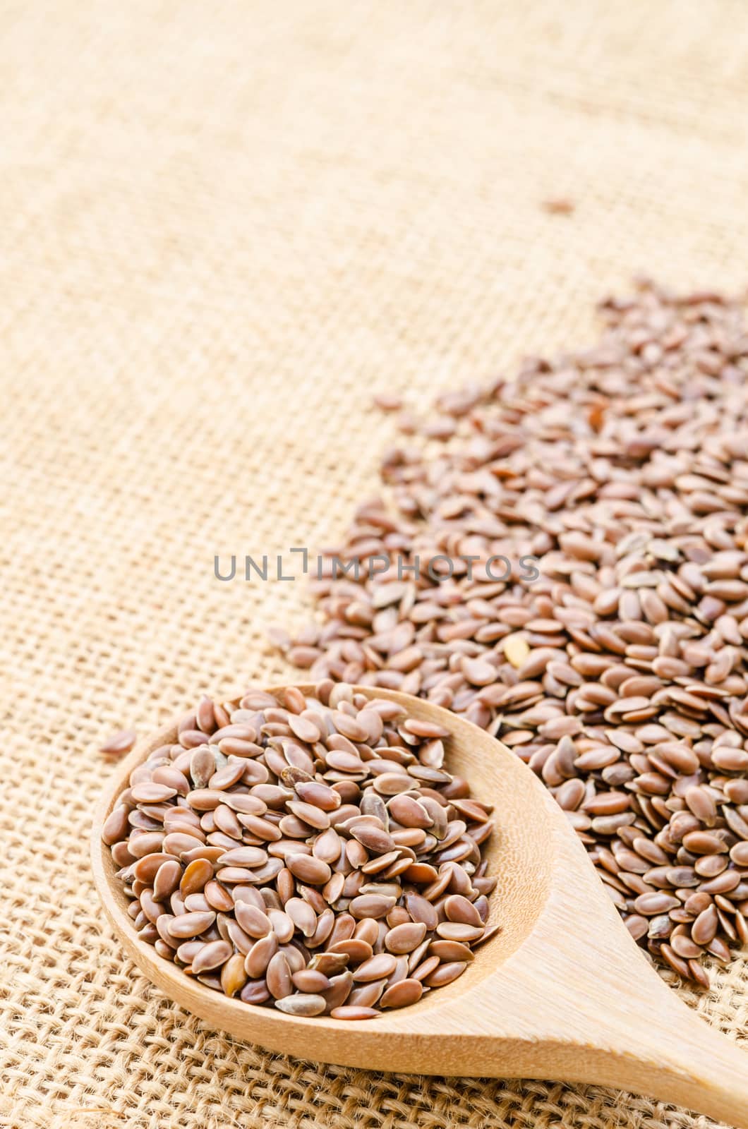 Heap of brown linseed, flax seeds with wooden spoon on sack background, concept for healthy nutrition