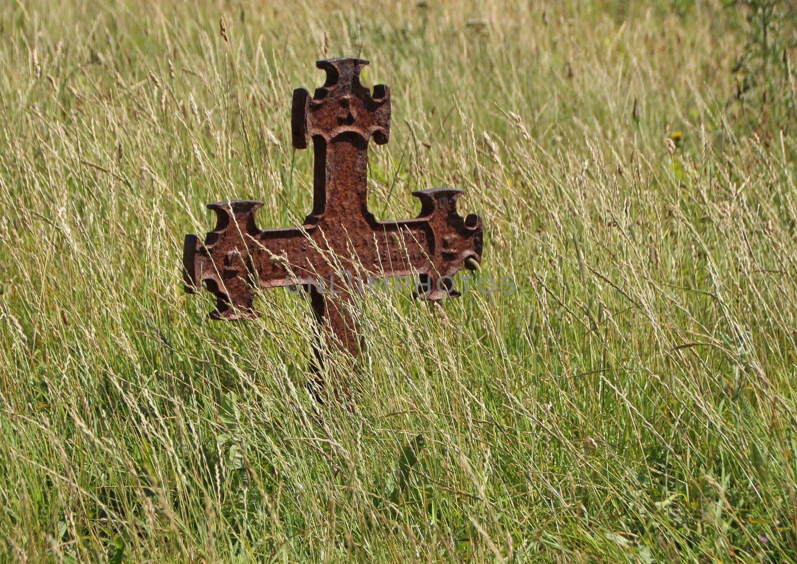 Isolated Rusty Iron Cross at Ancient Graveyard in Grass Field