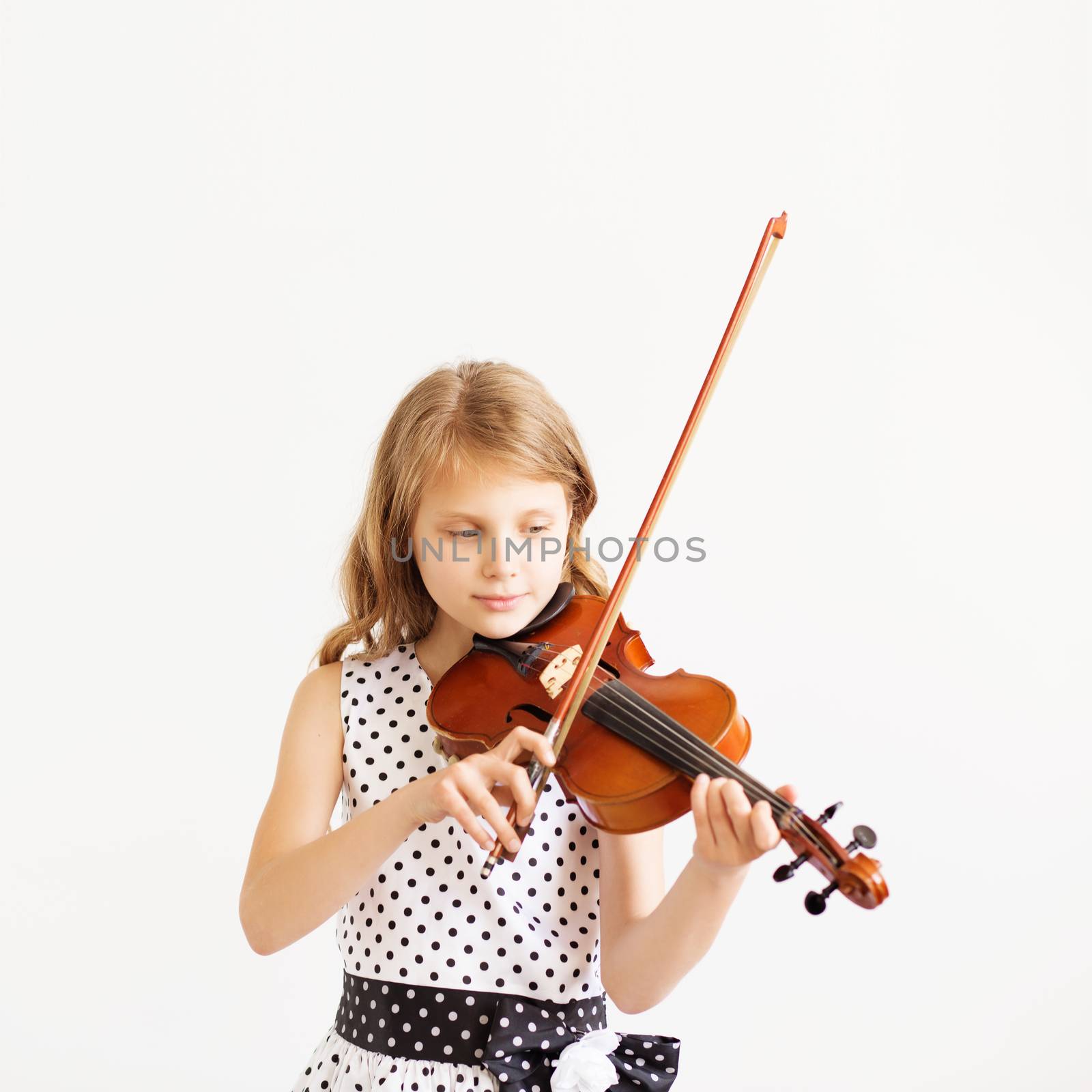 Portrait of girl with string and playing violin. Portrait of the little violinist. Beautiful gifted little girl playing on violin against the white background