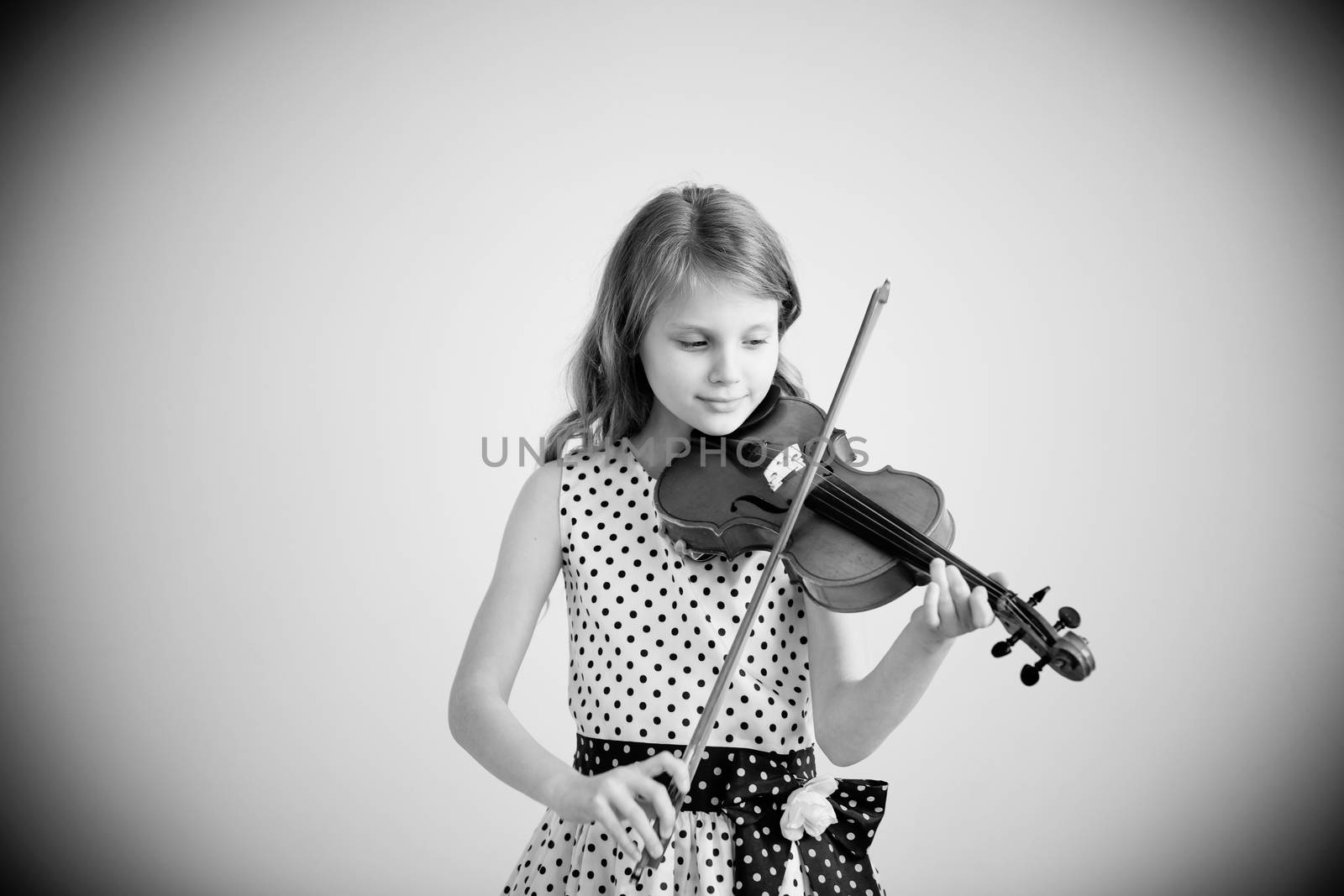 Portrait of girl with string and playing violin. Portrait of the little violinist. Beautiful gifted little girl playing on violin against the white background