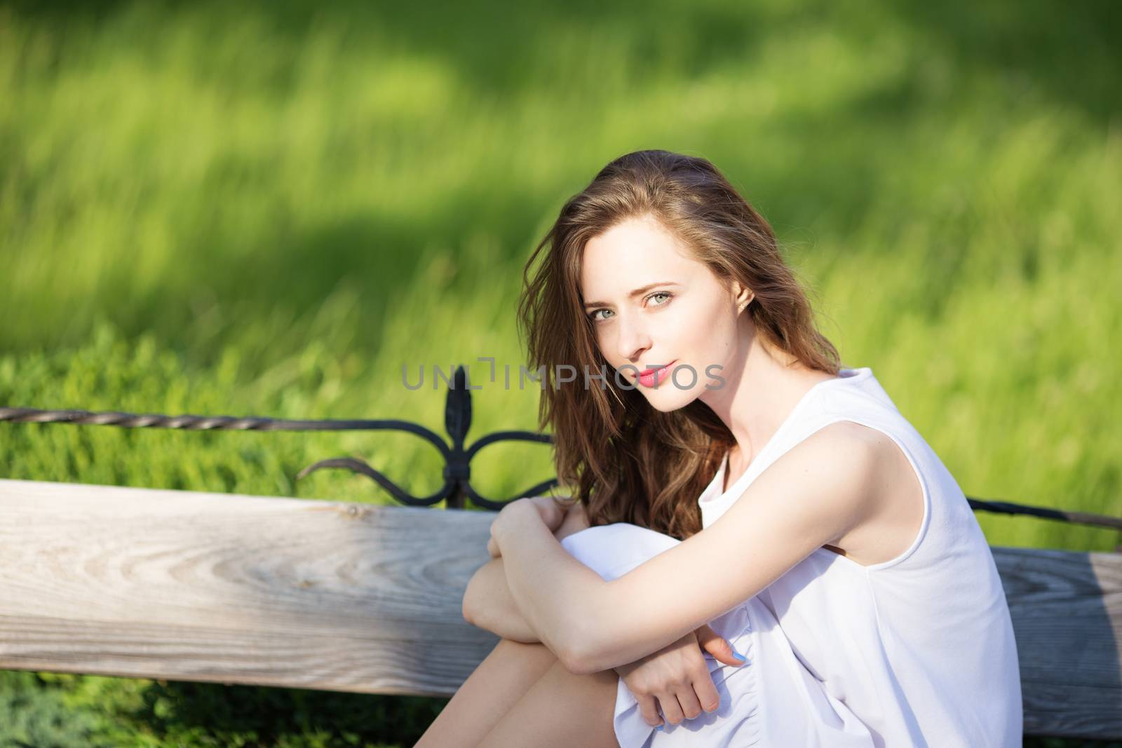 Portrait of lovely urban girl in short white dress in the street. Portrait of a happy smiling woman. Fashionable blonde girl sitting on a bench in a city park