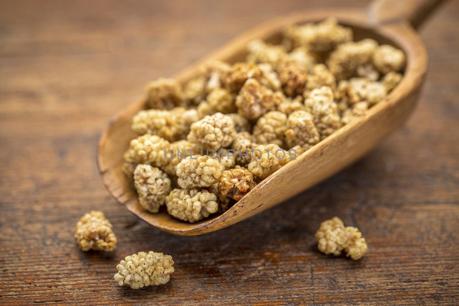 sun-dried white mulberry berries on a rustic wooden scoop against grunge wood, selective focus