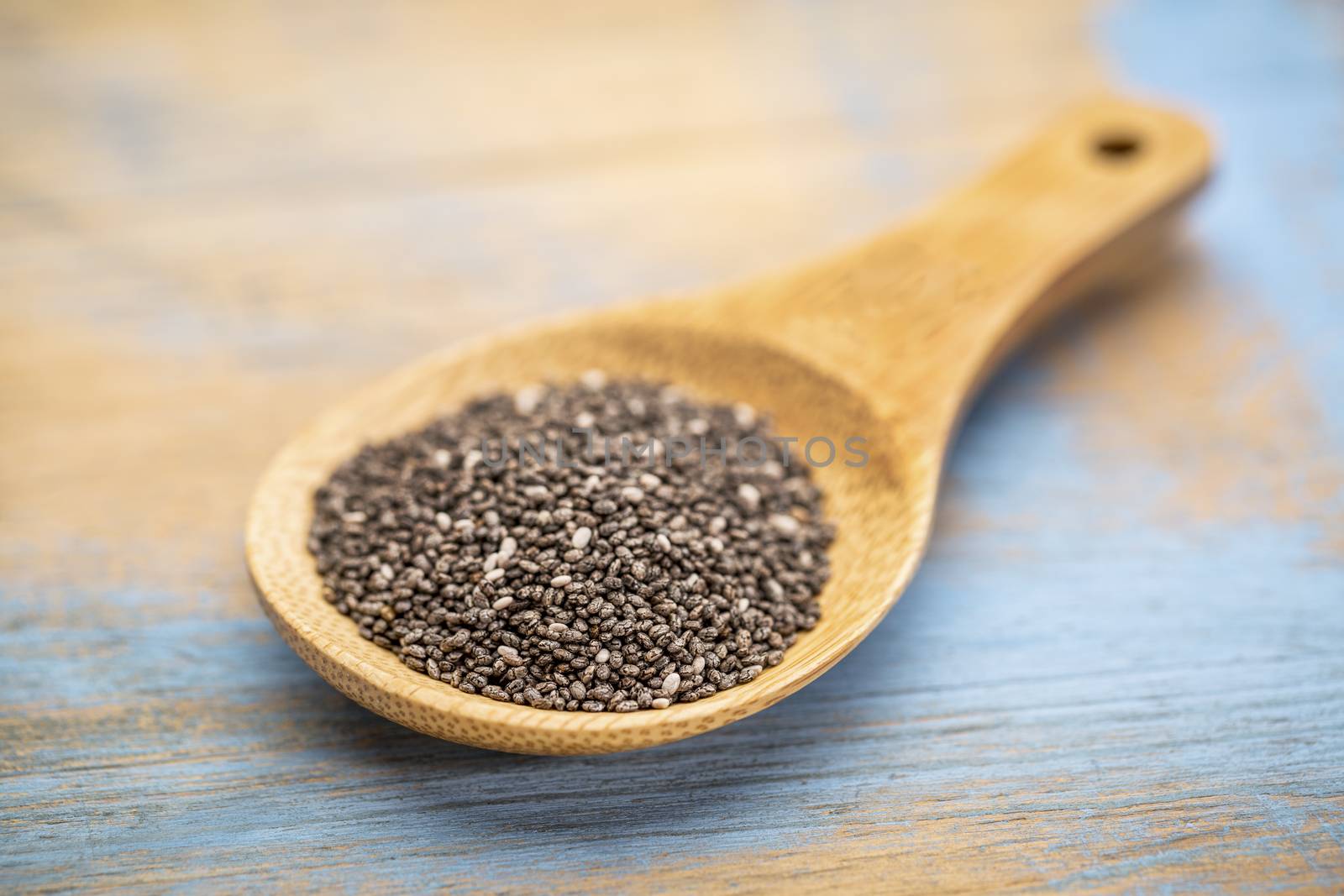 black chia seeds on a wooden spoon against blue painted grunge wood - selective focus