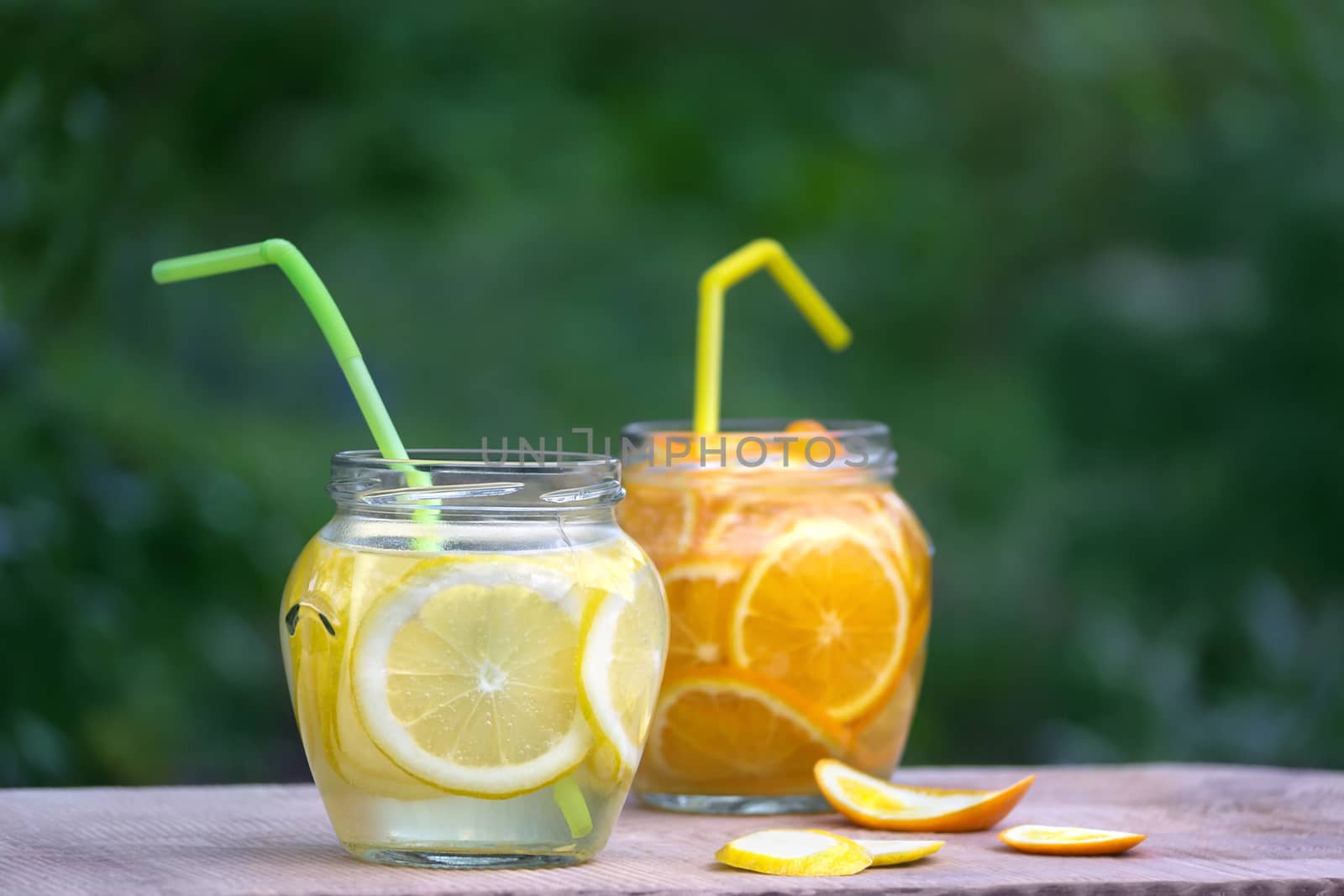 Lemonade in glass jars with tubes for cocktail on the blackboard in garden, on green blurred background