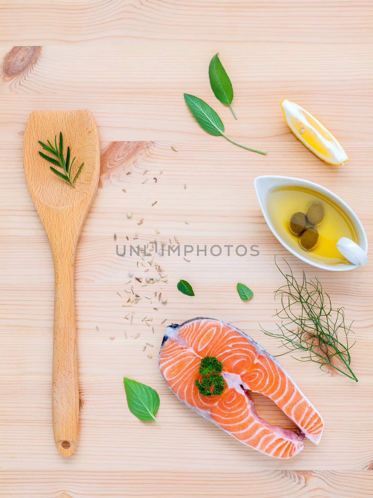 Raw salmon fillet in the white bowl with ingredients olive oil ,sea salt, and herbs  fennel ,sage ,rosemary ,garlic ,pepper and lemon for cooking on wooden background .