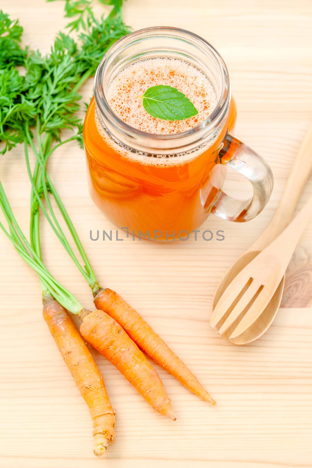 Glasses of carrot juice with carrot roots on wooden background.G by kerdkanno