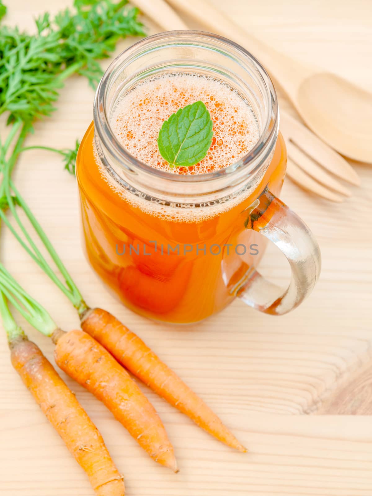 Glasses of carrot juice with carrot roots on wooden background.G by kerdkanno