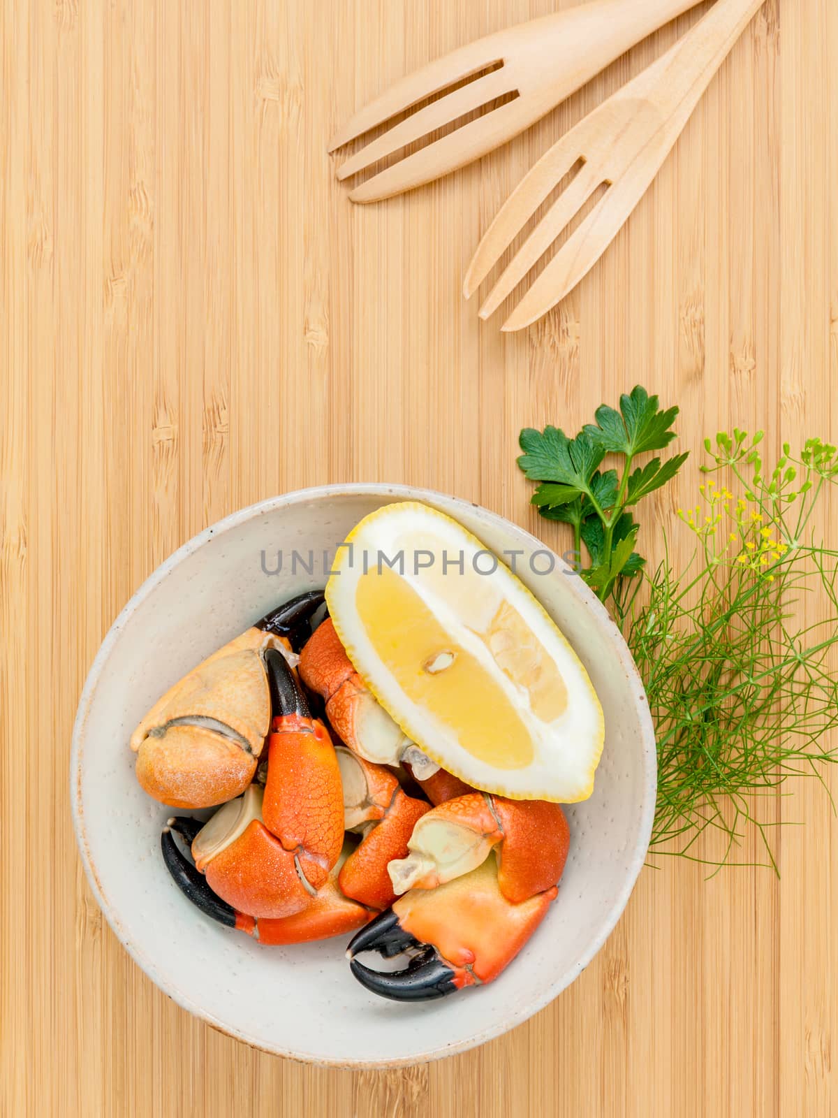 Fresh steamed red crabs leg in bowl . Red crabs leg with ingredients. Steamed red crabs leg with herbs Fennel ,parsley,rosemary,lemon and mint with fork on wooded cutting board.