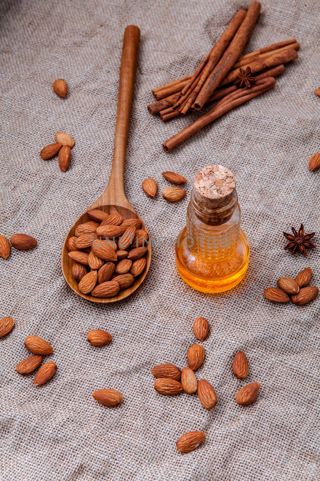 Bottle of extra virgin almonds oil with whole almonds and cinnamon sticks on hemp sack background.