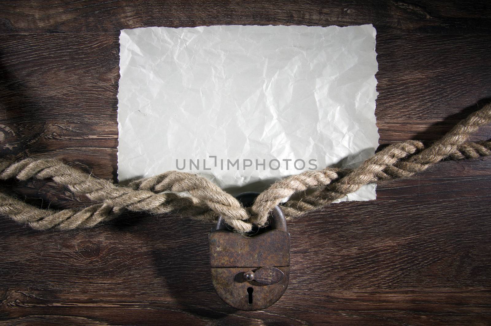 Old rusty lock with rope on wood background.