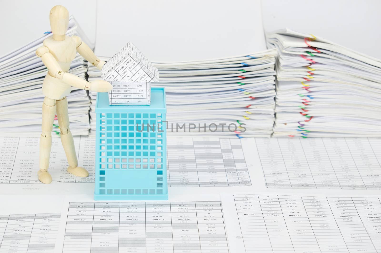 Wooden dummy holding house on blue basket with finance account have blur pile overload document of report with colorful paperclip as background.