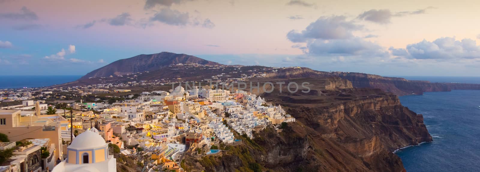 Cityscape of Fira, dramatically located on the edge of the caldera cliff on the island of Thira known as Santorini, Greece. Panorama shot at dusk.