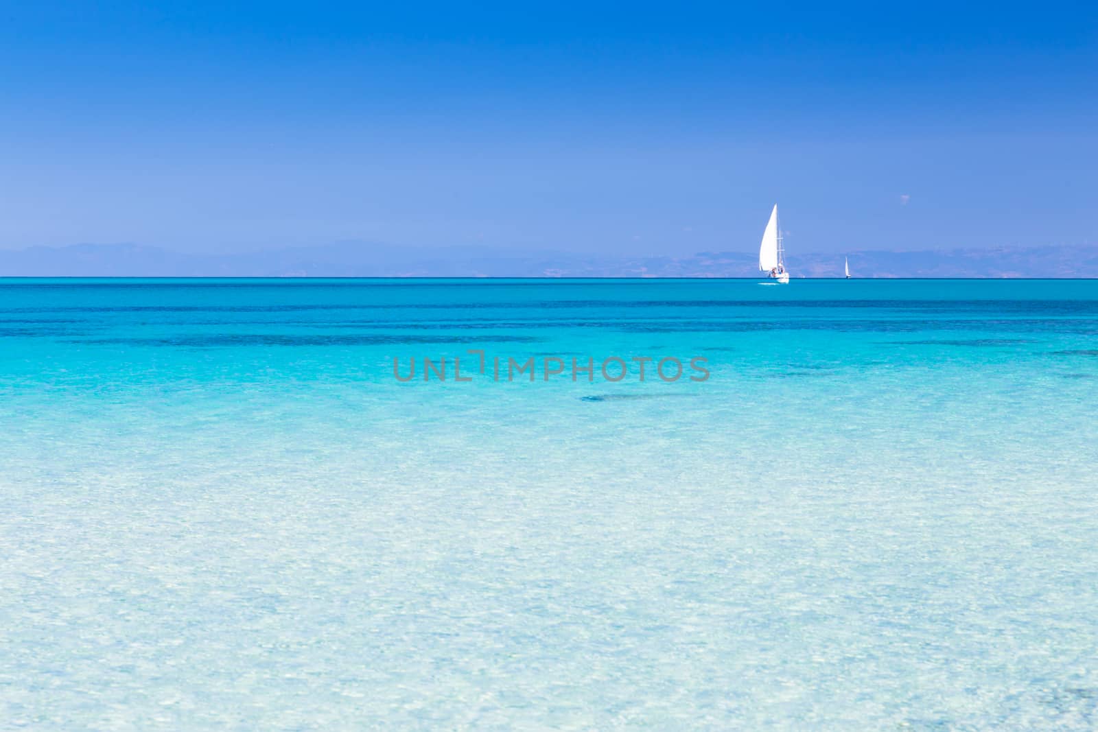 White sail boat at the beautiful turquoise blue mediterranean Pelosa beach near Stintino,Sardinia, Italy.