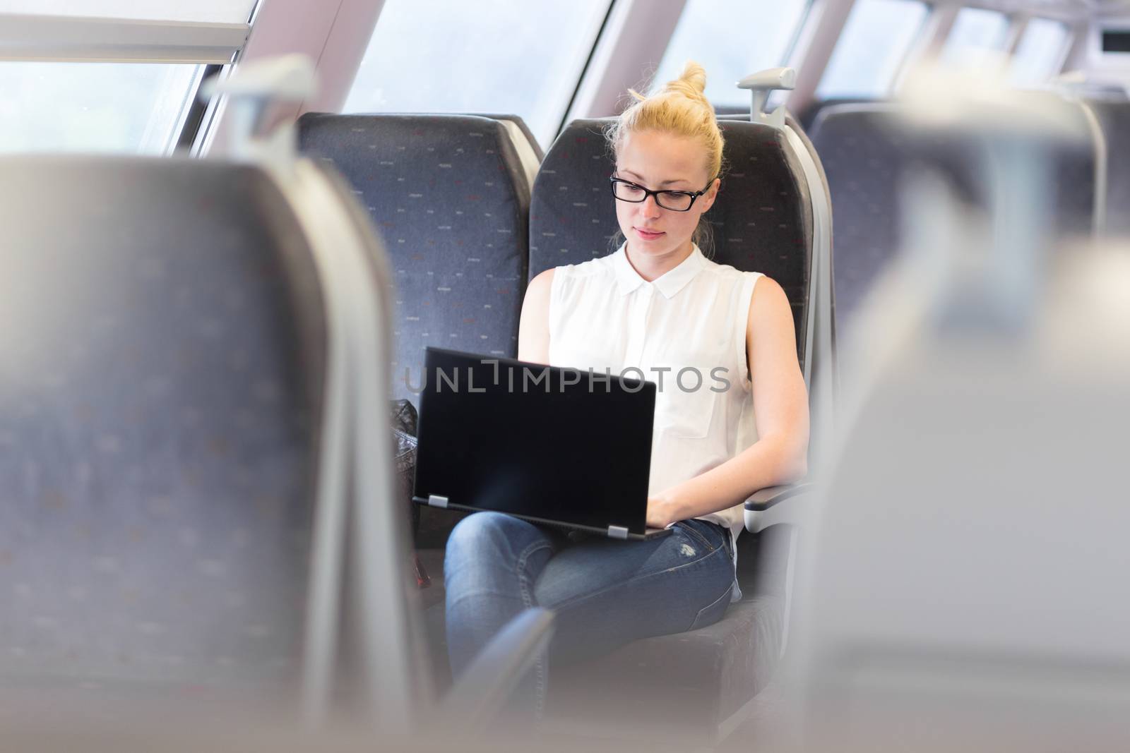 Woman travelling by train working on laptop. by kasto