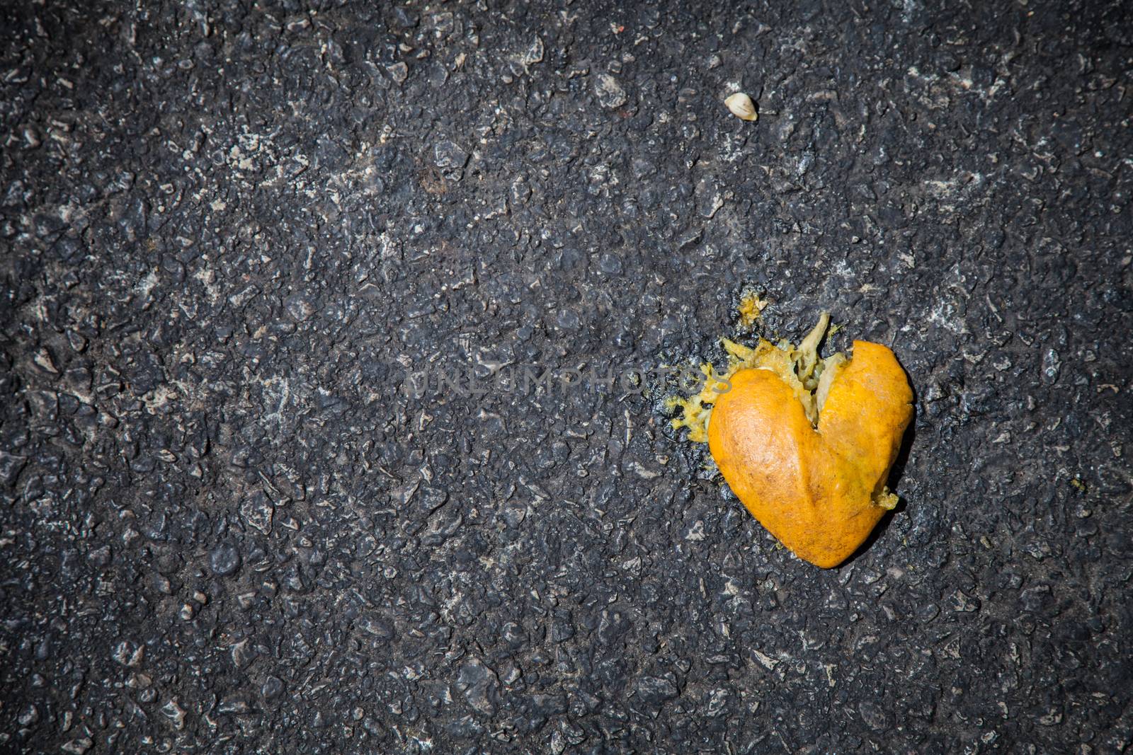 Smashed orange shaped like broken heart on the asphalt by evdayan