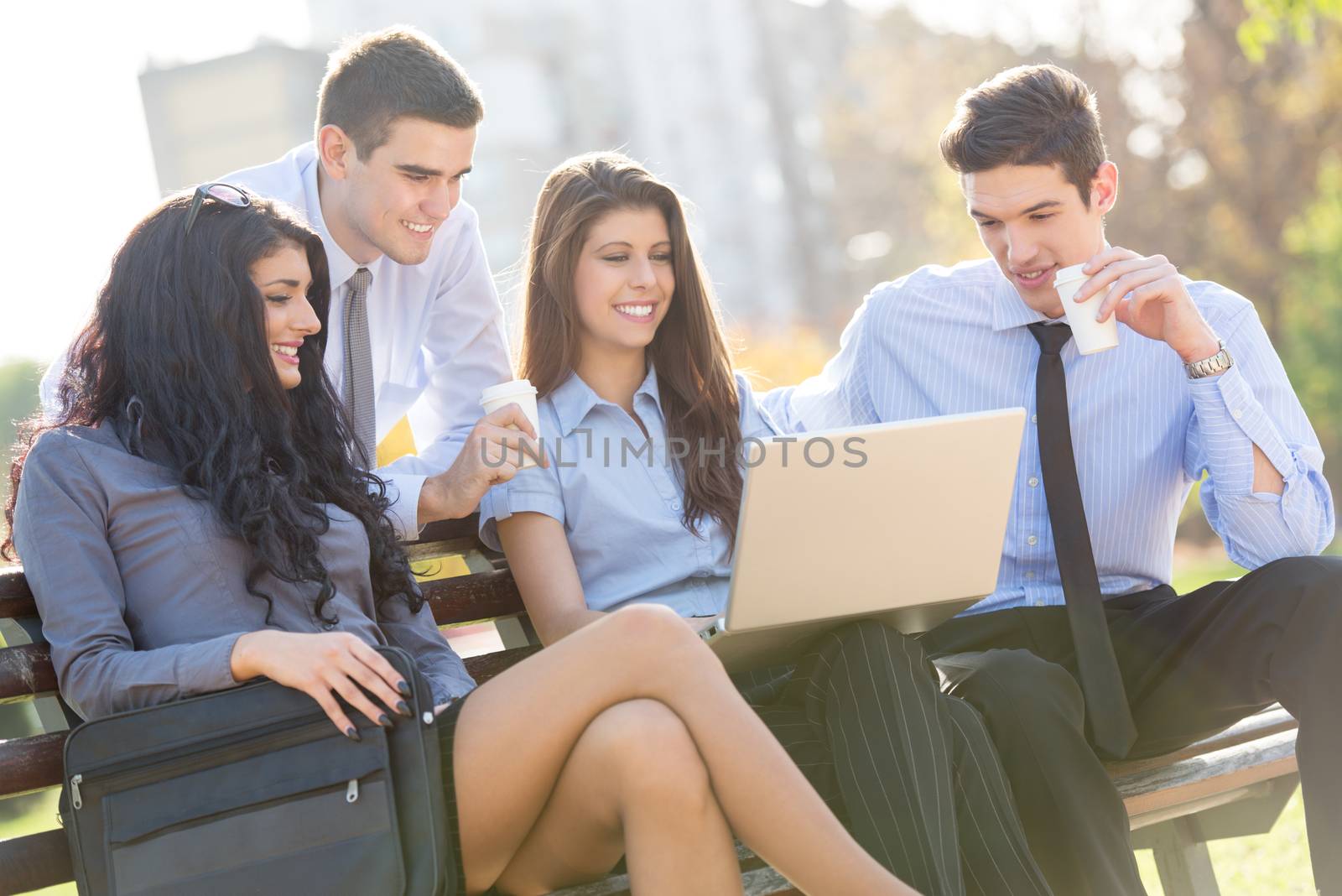 Small group of young business people sitting on a park bench during a break looking at the laptop.