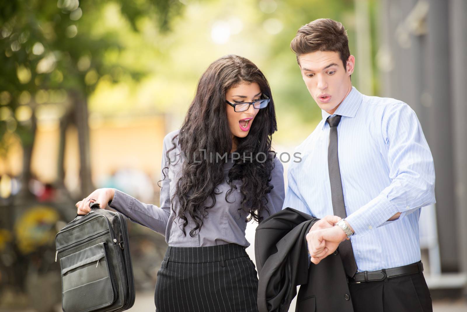 Couple of young business people, elegantly dressed, attractive businesswoman with glasses and a businessman, with an expression of astonishment on their faces, looking at businessman wristwatch.