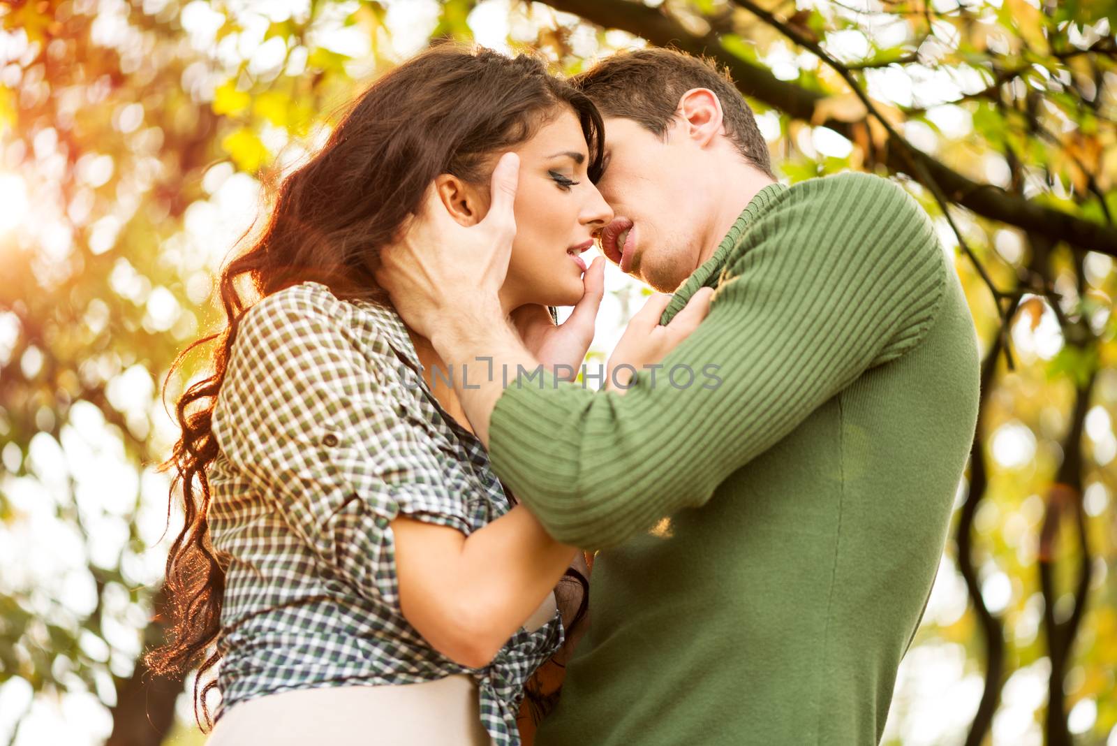 Kiss of beautiful brunette girl and handsome guy in the natural environment, while the sun shines through the trees.