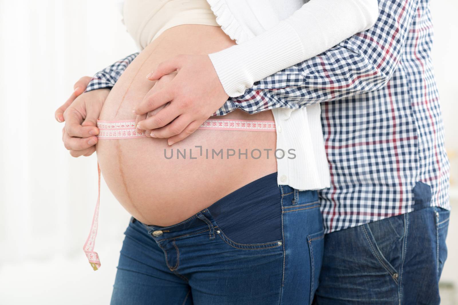 Male and female hands measuring on pregnant woman's belly .