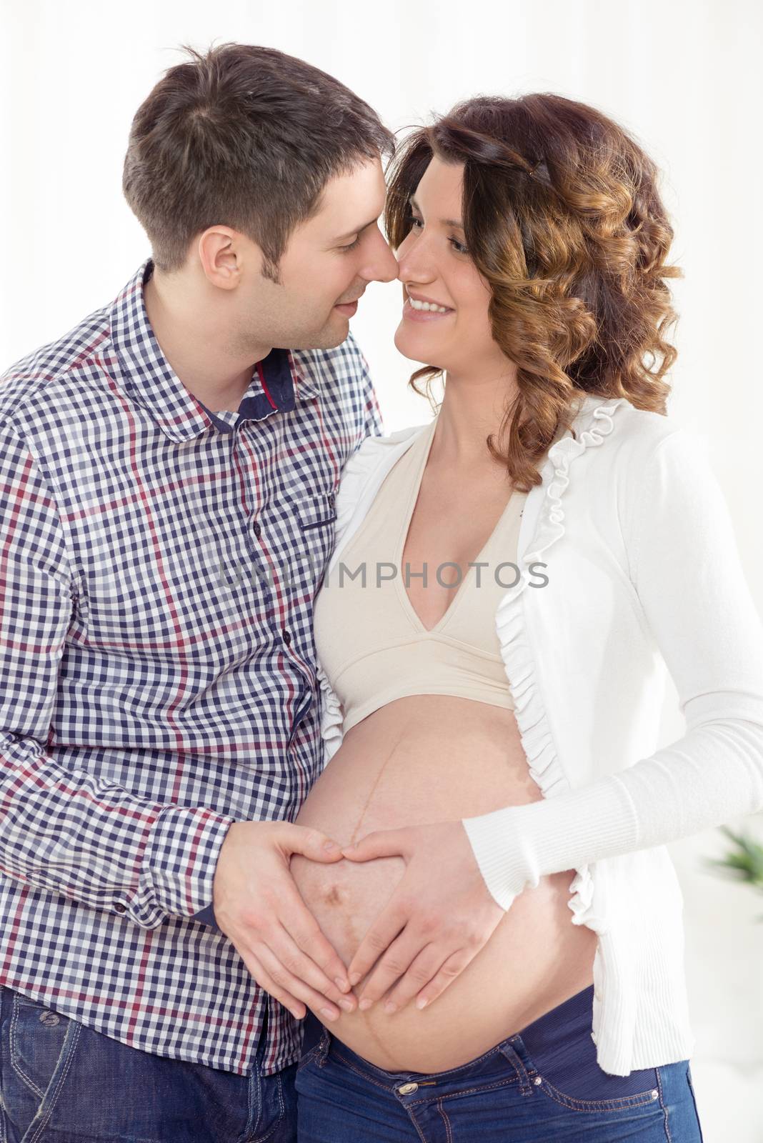 Portrait of a beautiful young couple making a heart shape on the woman's pregnant belly.