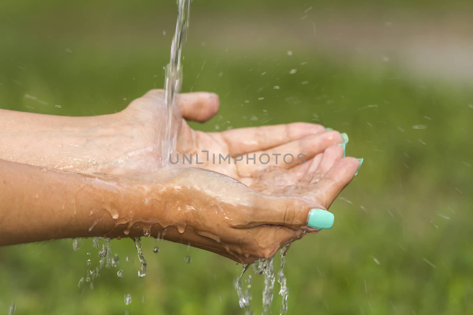 A stream of fresh clean water flowing to the hands of a girl with beautiful manicure