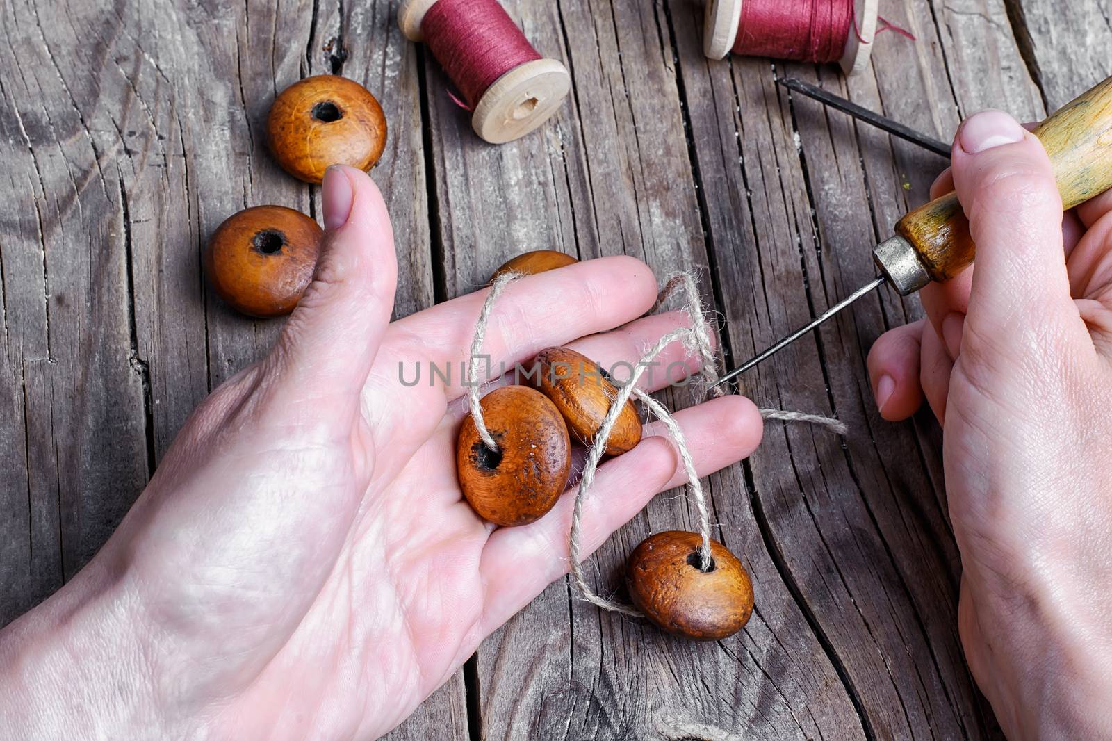 The hand with the awl naniniwala wooden beads on a string.