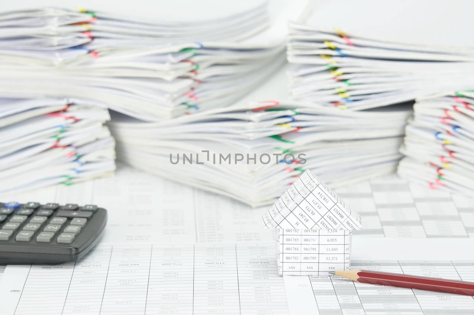 House and pencil on finance account have blur calculator and pile paperwork of report with colorful paperclip as background.