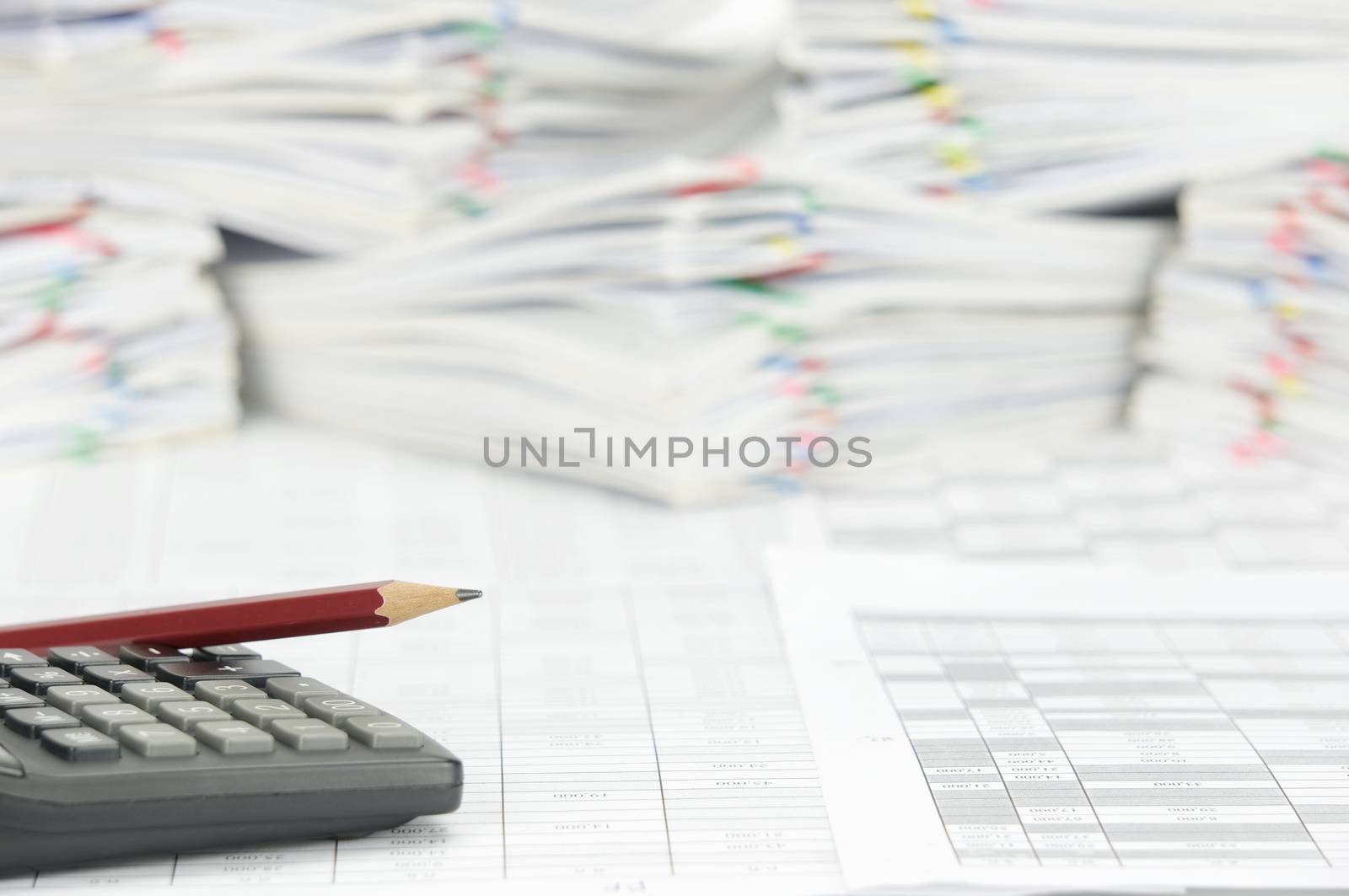 Pencil place on calculator with finance account have blur pile paperwork of report with colorful paperclip as background.