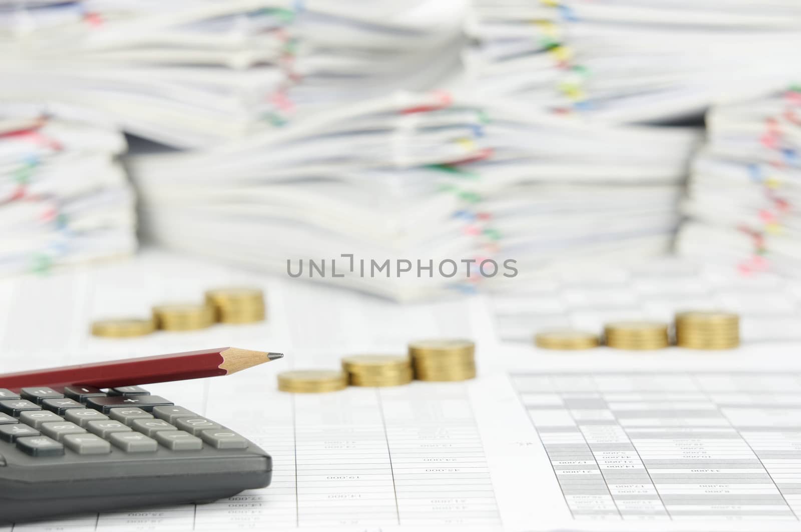 Pencil place on calculator with finance account have blur step pile of gold coins and pile paperwork of report with colorful paperclip as background.