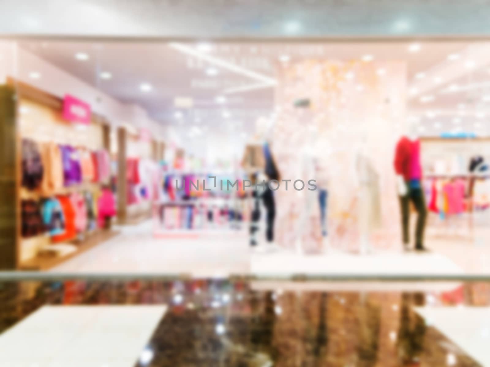 Blur image of window bright display with four mannequins wearing red dress with text Sale