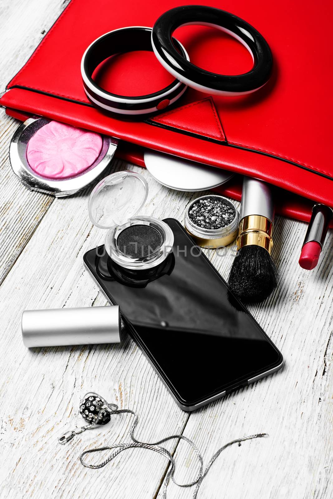 Fashionable ladies handbag with cosmetics and phone on light background