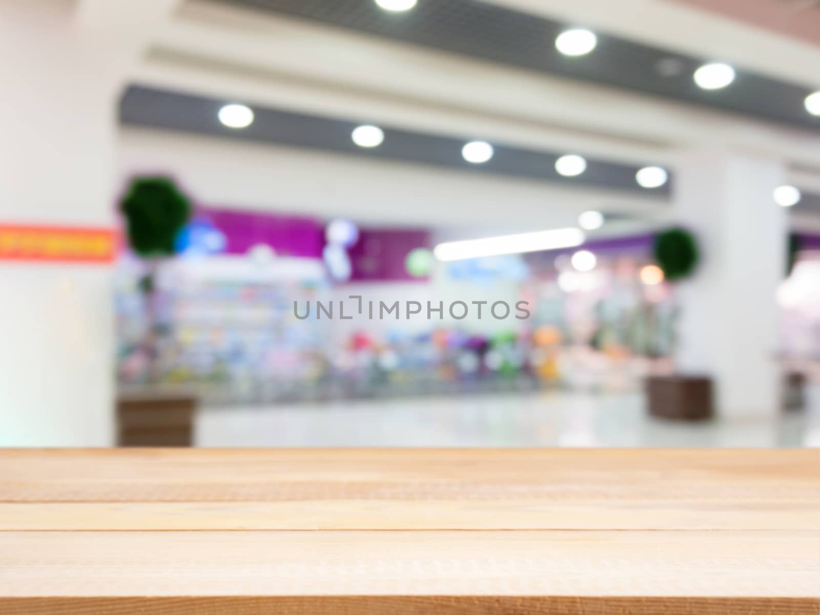 Wooden board empty table in front of blurred background. Perspective light wood table over blur in shopping mall hall. Mock up for display or montage your product.